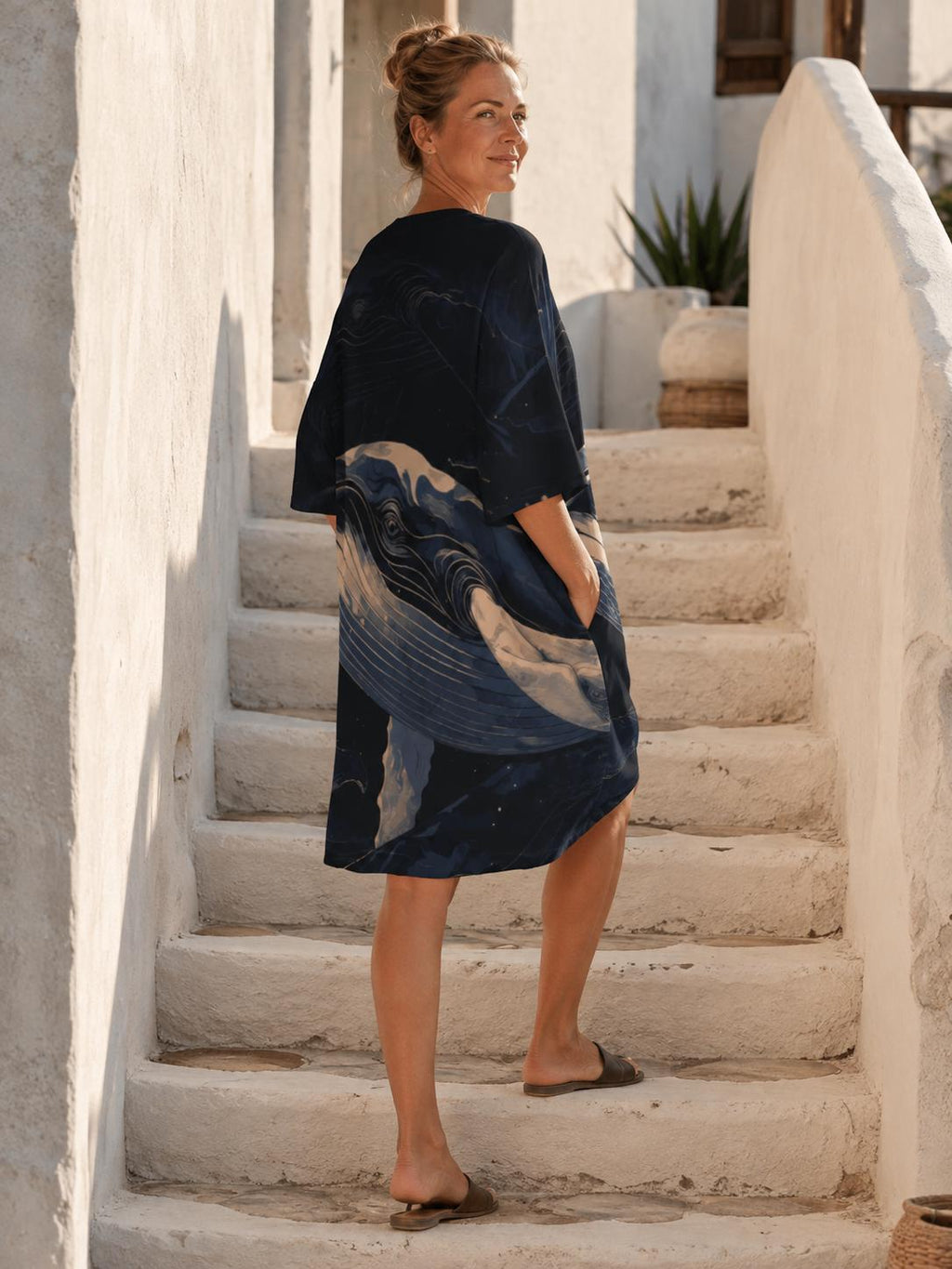 May include: A dark navy blue knee-length dress featuring a large, stylized graphic print of a whale in shades of light blue and cream. The dress has short, wide sleeves, a round neckline, and visible side pockets, with a loose, flowing silhouette.