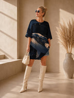 May include: A dark blue oversized t-shirt dress featuring a graphic print of a whale in shades of light blue and white. The garment has short sleeves and a round neckline. It is paired with cream-colored knee-high boots and a small woven handbag.