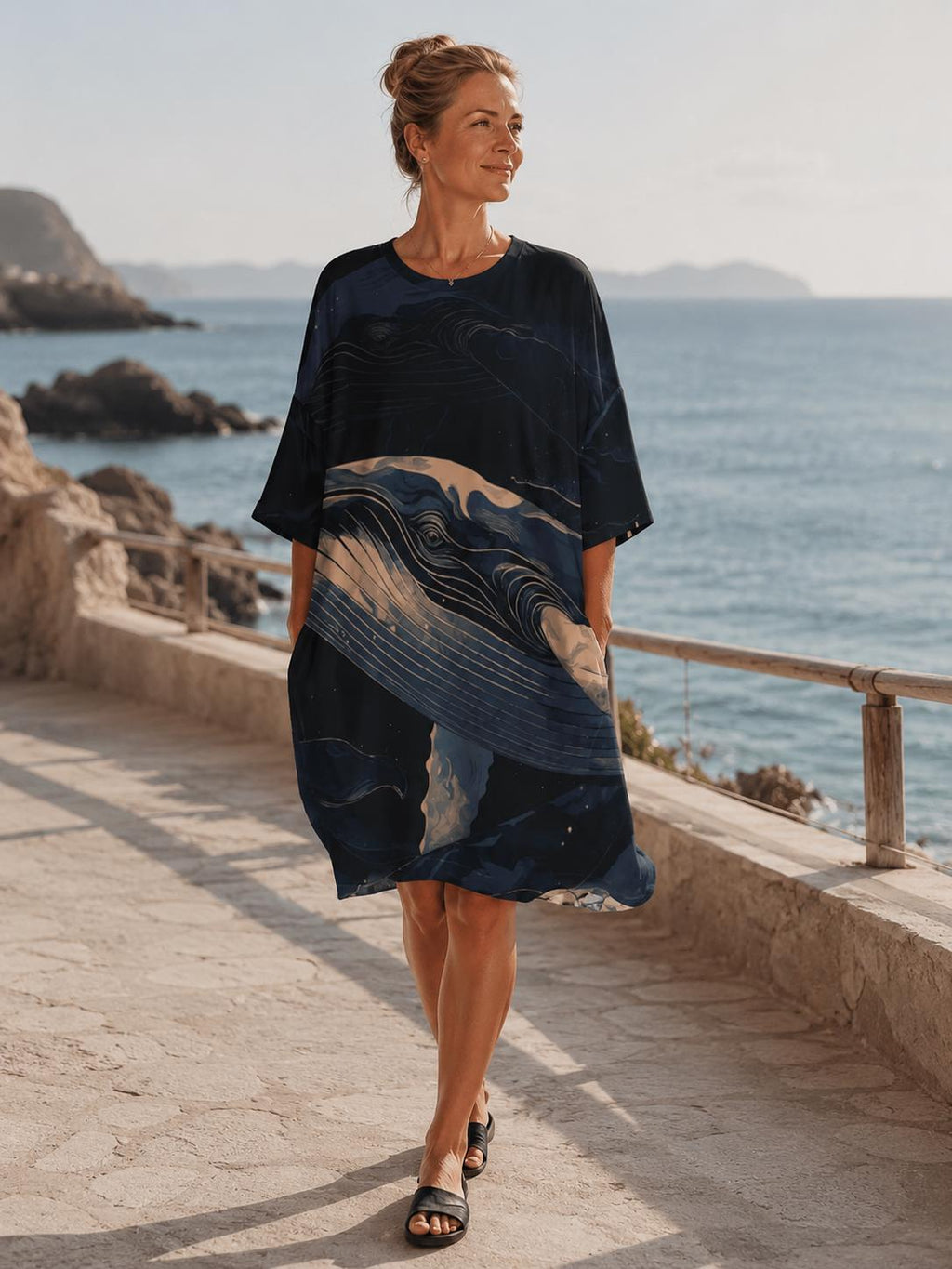 May include: A knee-length, short-sleeved dress in a dark navy blue hue, featuring a prominent abstract graphic print of a whale in shades of cream, light blue, and dark blue. The garment has a round neckline and a loose, relaxed silhouette.