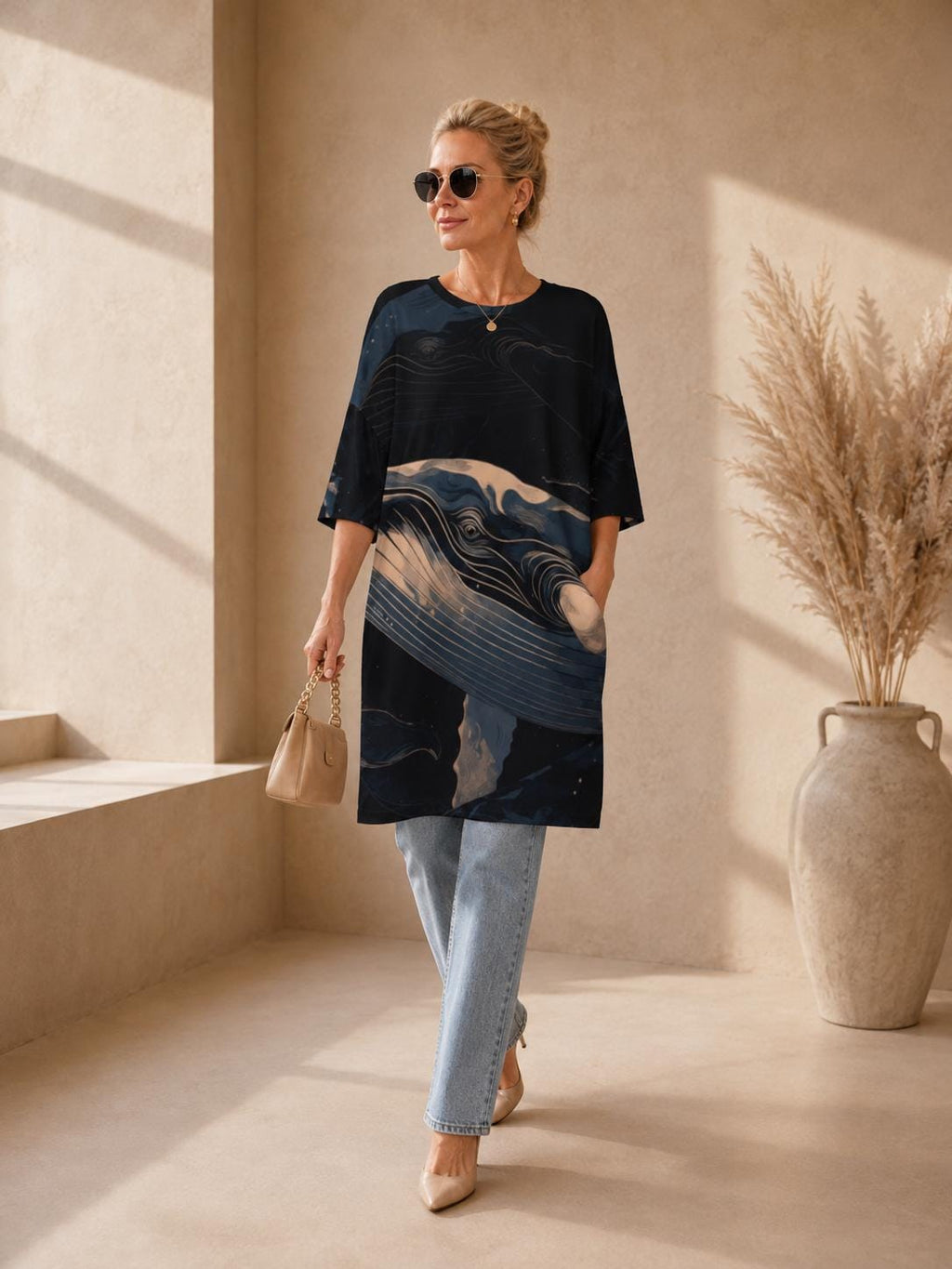 May include: A black tunic featuring a large, detailed graphic of a whale in shades of blue, cream, and dark navy. The garment has a round neckline, elbow-length sleeves, and a straight hemline. It is paired with light blue denim jeans.