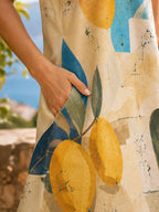 May include: A beige sleeveless dress featuring a vibrant print of yellow lemons and dark green leaves, accented with abstract blue geometric shapes and thin black line drawings. The garment includes a functional side pocket.