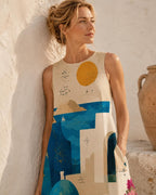 May include: A sleeveless beige dress featuring a graphic print of a coastal landscape with a yellow sun, blue sea, white buildings, and a small sailboat. The design includes dark blue architectural arches and scattered star-like constellations.